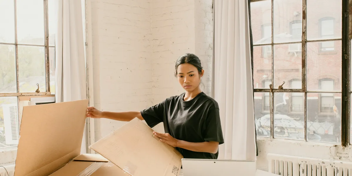 A shop owner folds a cardboard box to pack an order in a sunlit loft