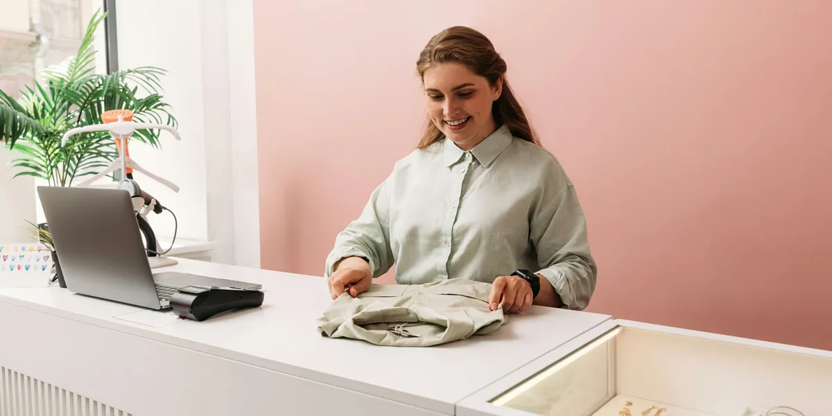 A boutique owner folds a garment at the counter of her small shop