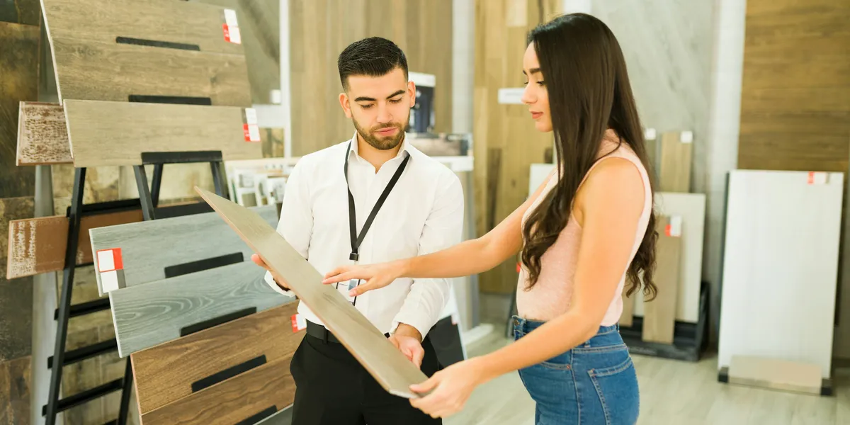 A salesperson shows a customer a wood flooring sample in a showroom