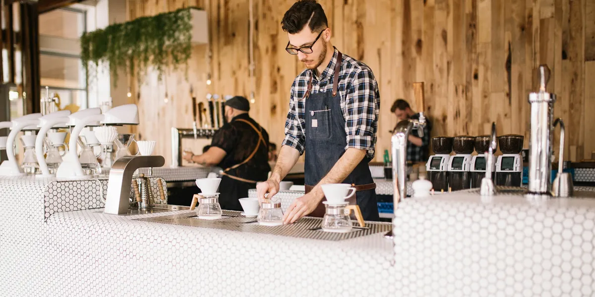 A café owner prepares pour-over coffee behind a white-tiled counter
