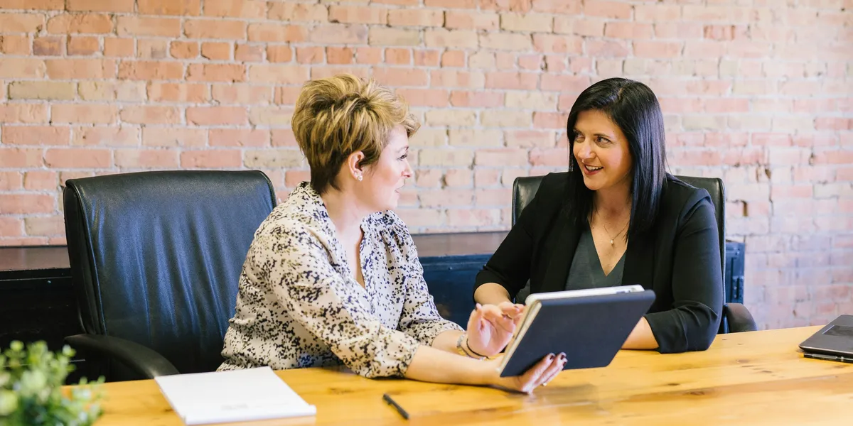 An adviser goes through figures on a tablet with a client at a wooden table