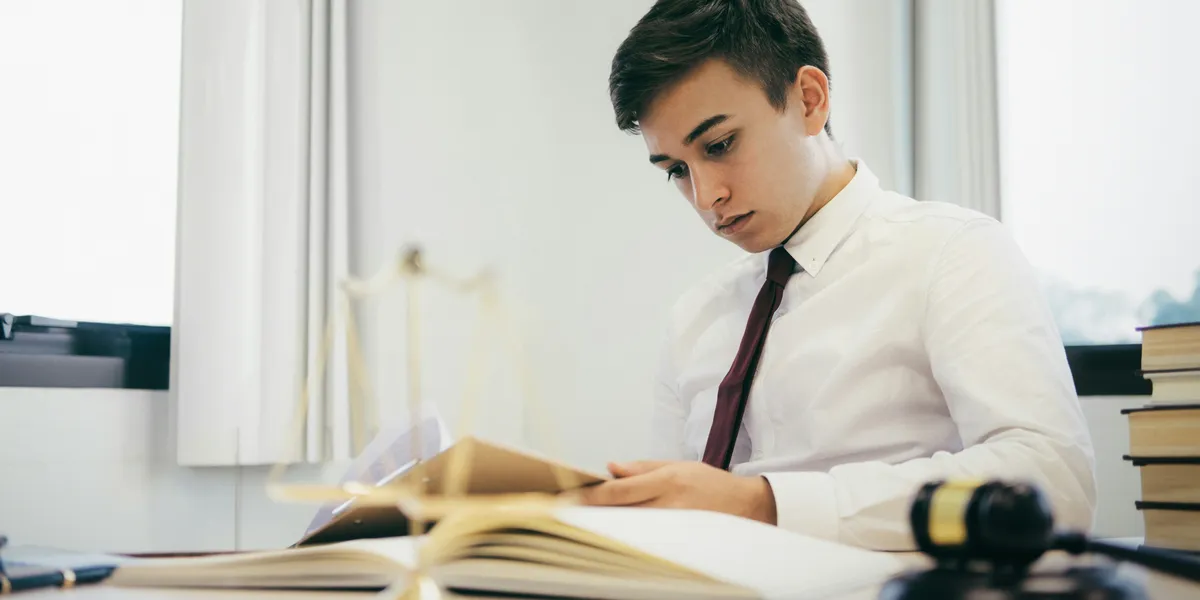A young lawyer reading through papers at his desk beside a gavel and law books