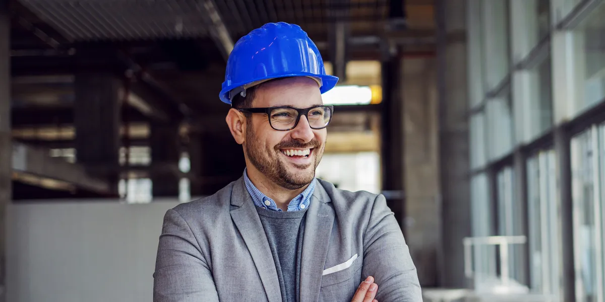 A smiling manager in a hard hat and blazer inside a building under construction