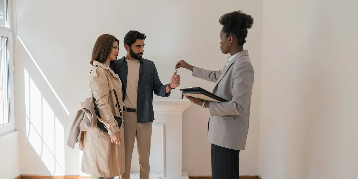 An estate agent handing a couple the keys in an empty, sunlit room