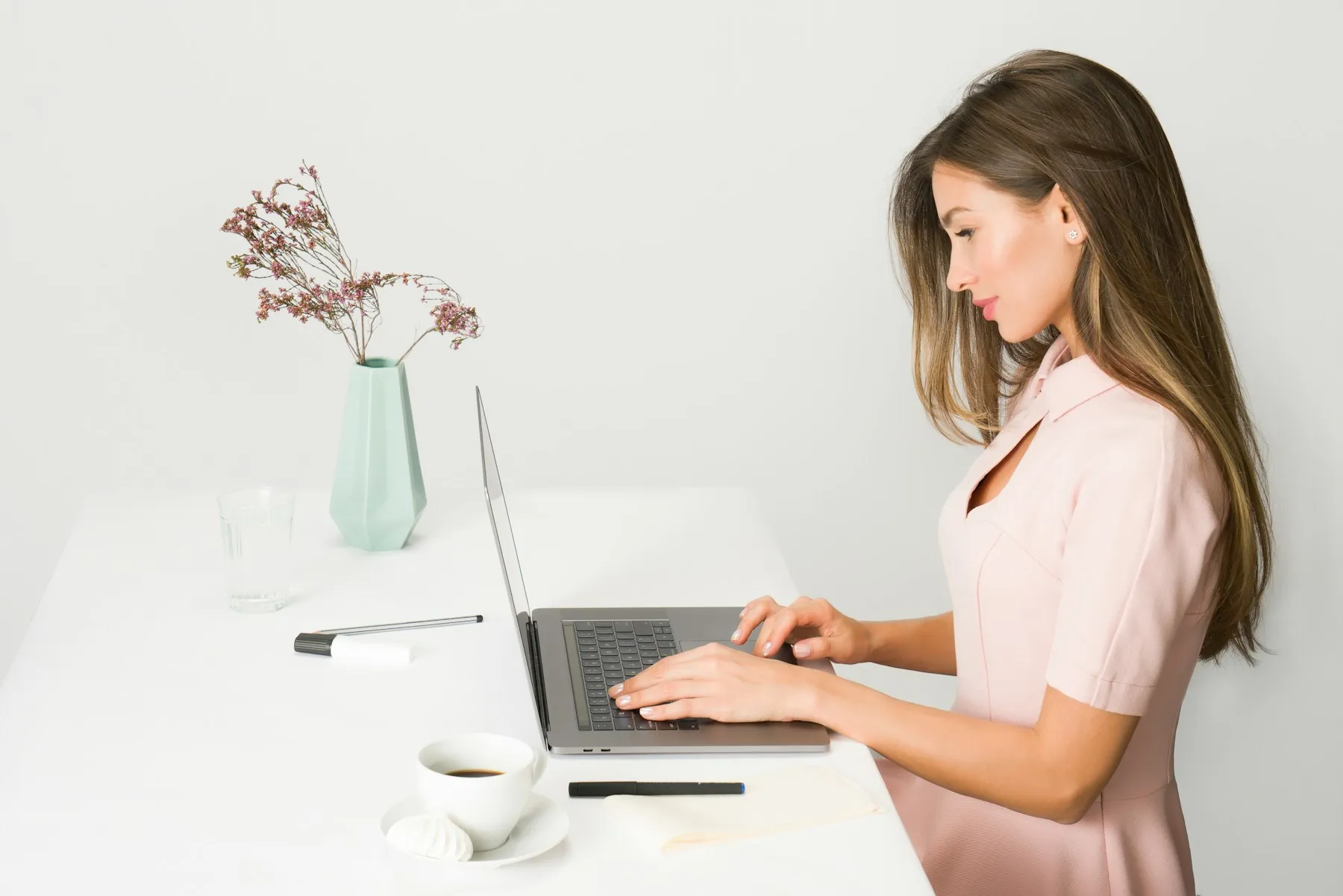 A woman working on a laptop at a bright white desk